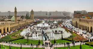 Erbil / Hewler / Arbil / Irbil, Kurdistan, Iraq: main square, Shar Park, with crowds enjoying the pleasantly cool area created by the fountains - arcades on both sides and Nishtiman mall in front - Mosque and Erbil Clocktower on the left - dense traffic on Kirkuk avenue on the right - seen from the Erbil citadel - photo by M.Torres